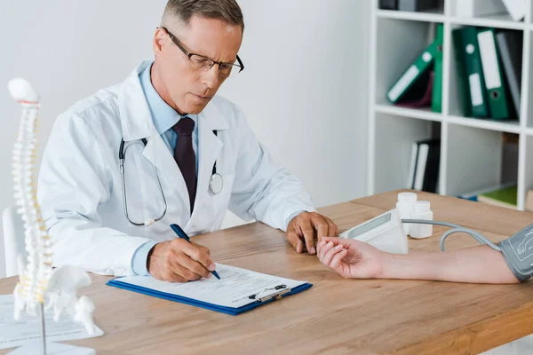 Médico guapo medir la presión arterial del paciente en la clínica - foto de stock