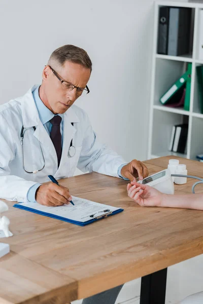 Médico em óculos medir a pressão arterial da mulher no hospital — Fotografia de Stock