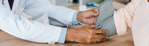 Panoramic shot of doctor measuring blood pressure of woman in hospital — Stock Photo