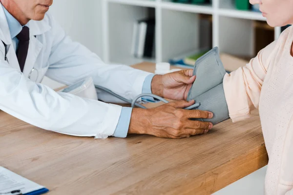 Vista recortada del médico que mide la presión arterial de la mujer en la mesa en el hospital — Stock Photo