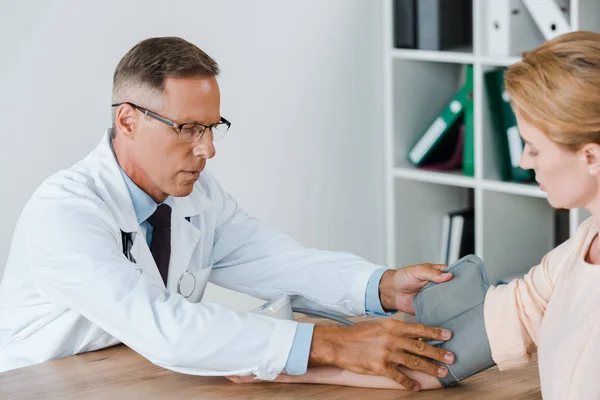 Fuoco selettivo del medico che misura la pressione sanguigna della donna sul tavolo in ospedale — Stock Photo