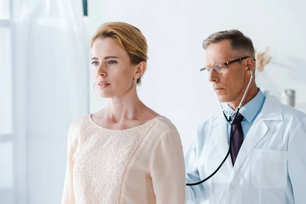Handsome doctor in glasses examining attractive woman in clinic — Stock Photo