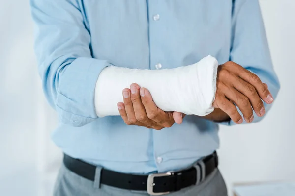 Vista ritagliata di uomo ferito toccare braccio rotto avvolto in benda di gesso — Foto stock