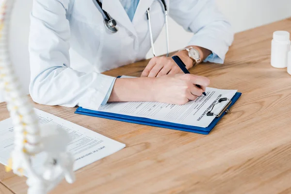 Cropped view of doctor writing diagnosis on wooden table — Stock Photo