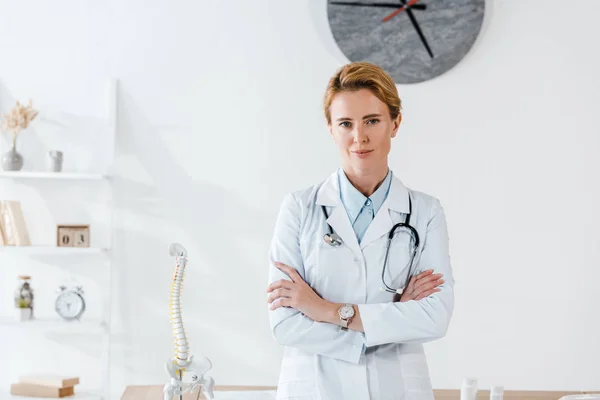 Attractive doctor standing with crossed arms in hospital — Stock Photo