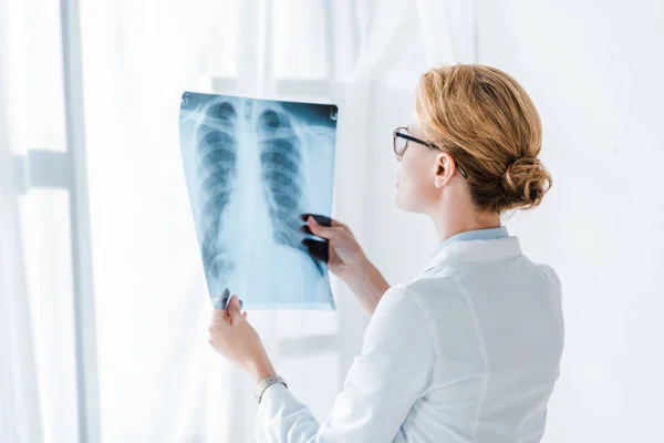 Doctor in glasses looking at x-ray while standing in clinic — Stock Photo