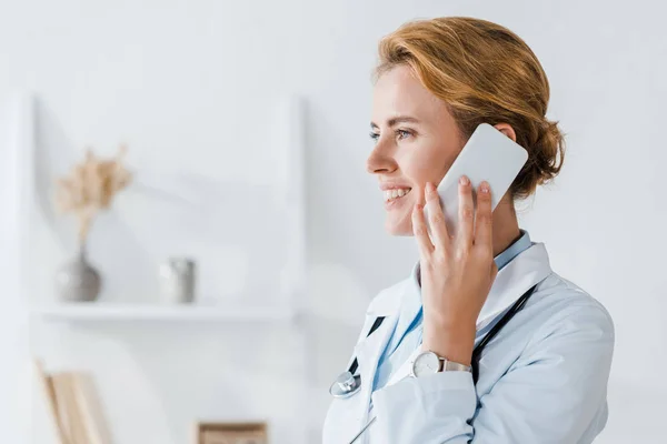 Щасливий лікар посміхається під час розмови на смартфоні в клініці — стокове фото