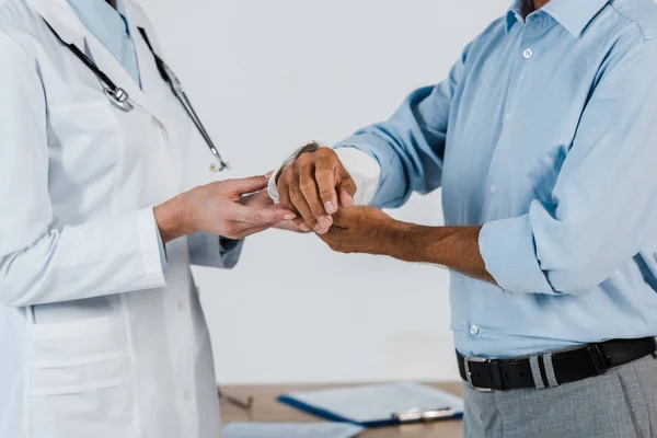 Cropped view of doctor touching broken arm on patient in clinic — Stock Photo