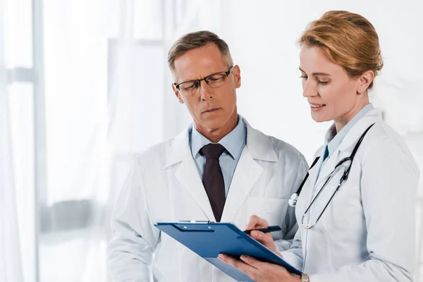 Handsome man in glasses looking at clipboard near coworker — Stock Photo