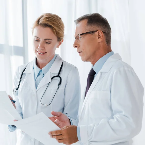 Handsome man in glasses looking at paper near coworker — Stock Photo