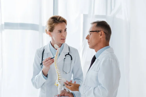 Attraente medico che tiene modello di colonna vertebrale vicino collega in occhiali — Foto stock