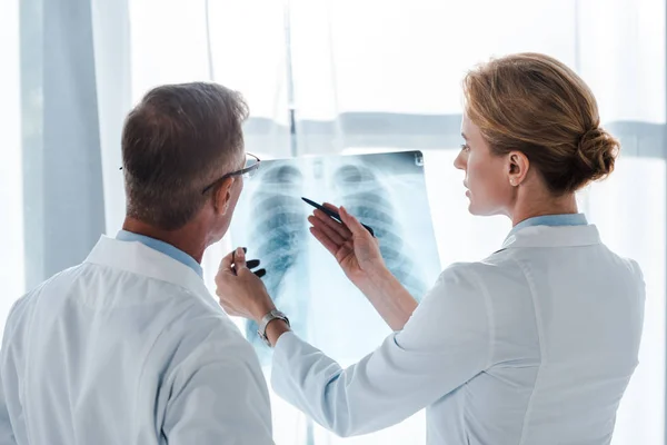 Attraktive Ärztin mit Stift und Röntgenbild in der Nähe ihres Kollegen — Stockfoto