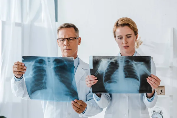 Médico en gafas y atractivo compañero de trabajo mirando rayos X en la clínica - foto de stock