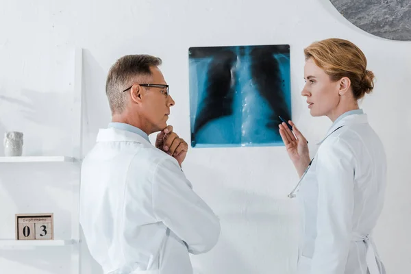 Лікар в окулярах торкаючись обличчя і дивлячись на жест колеги поблизу рентгенівського променя — стокове фото