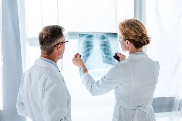 Доктор в очках смотрит на рентген в руках коллеги — стоковое фото