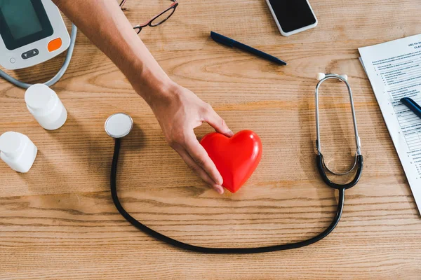 Recortado vista de la mujer sosteniendo rojo modelo de corazón cerca de teléfono inteligente - foto de stock