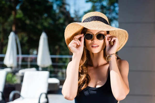 Hermosa chica sexy en traje de baño, gafas de sol y sombrero de paja posando en el resort - foto de stock