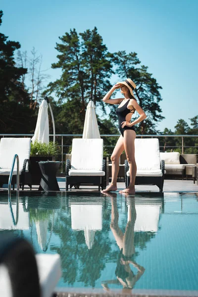 Schöne Frau in Badeanzug und Strohhut posiert in der Nähe von Schwimmbad auf Resort — Stockfoto