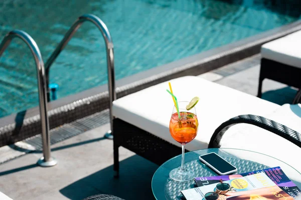 Table with cocktail, magazines and sunglasses near swimming pool on resort — Stock Photo