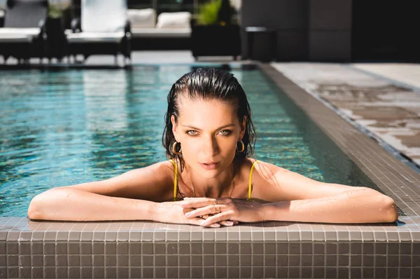 Atractiva mujer sexy posando en la piscina en el complejo y mirando a la cámara - foto de stock