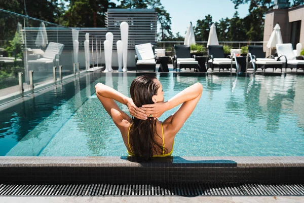 Вид сзади на сексуальную женщину, расслабляющую руки на голове в бассейне на курорте — стоковое фото