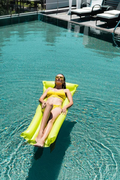 Vista de ângulo alto da menina bonita que nada no colchão inflável na piscina no recurso — Fotografia de Stock