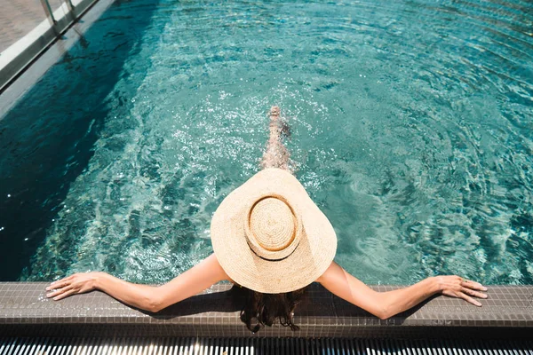 Vue arrière sur femme en chapeau de paille relaxant dans la piscine — Photo de stock