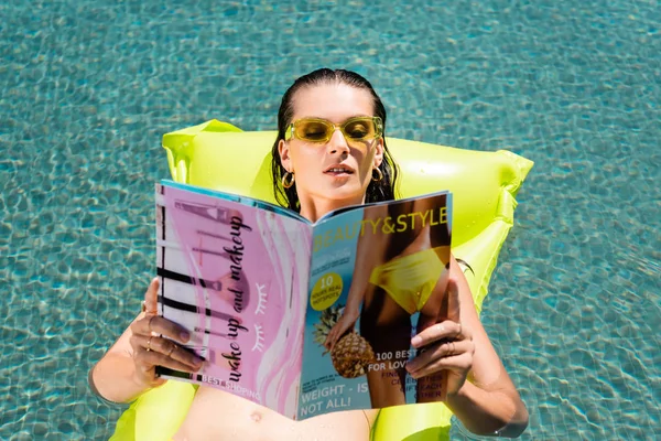 Menina bonita no colchão inflável na piscina e revista de leitura no recurso — Fotografia de Stock