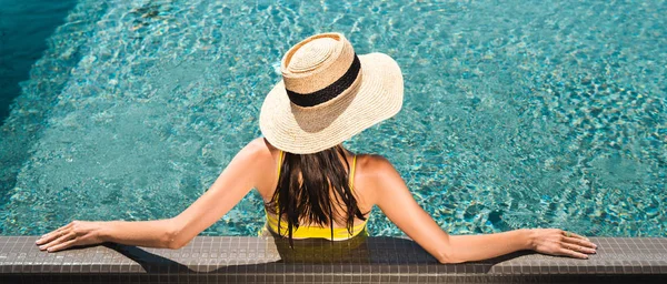 Vue arrière sur femme en chapeau de paille relaxant dans la piscine, vue panoramique — Photo de stock