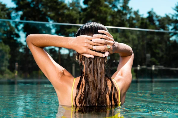 Back view of woman in swimming in pool on resort touching hair during daytime — Stock Photo