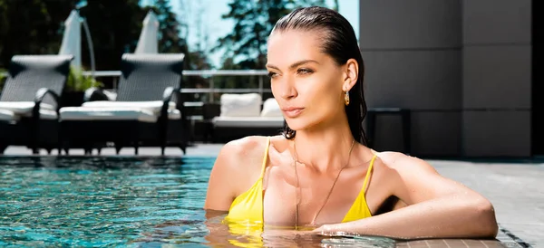 Tiro panorâmico de bela mulher sexy em maiô relaxante na piscina no resort — Fotografia de Stock