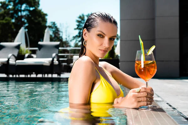 Beautiful girl in swimming suit with cocktail on resort in swimming pool — Stock Photo