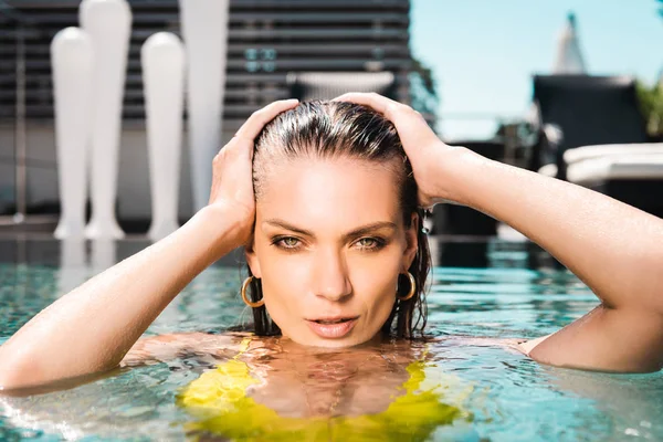 Hermosa mujer sexy con las manos en la cabeza posando en la piscina en el complejo - foto de stock