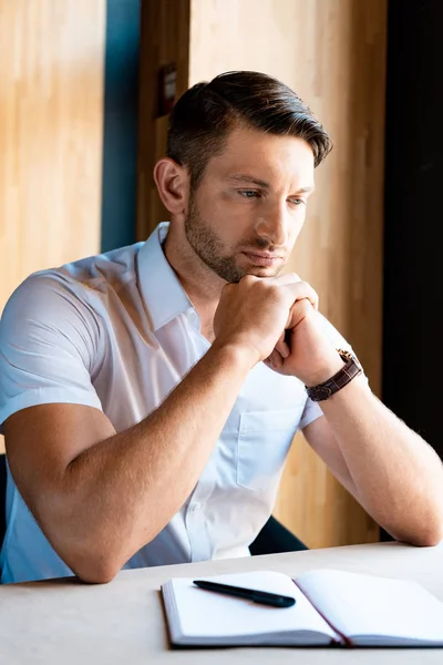 Pensive muscular man sitting with clenched hands in cafe — Stock Photo