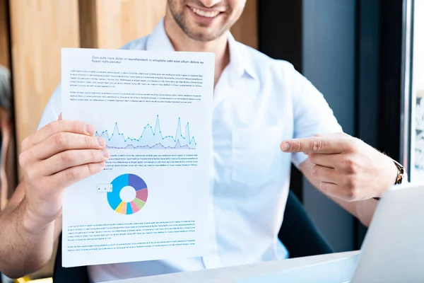 Vista ritagliata dell'uomo sorridente che punta con il dito al documento con il diagramma nel caffè — Foto stock