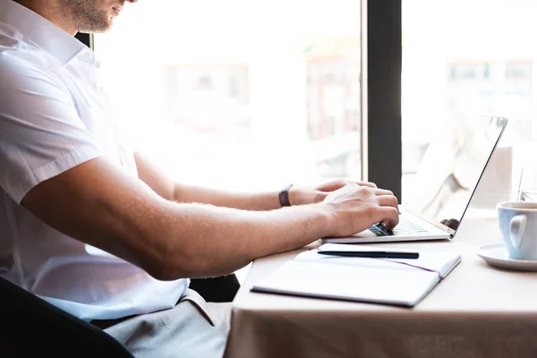 Vista recortada del hombre escribiendo en el teclado del ordenador portátil en la cafetería - foto de stock