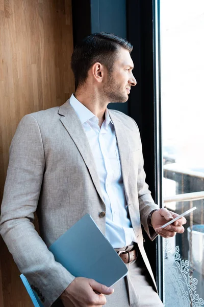 Nachdenklicher Geschäftsmann hält Ordner und Smartphone im Café — Stockfoto