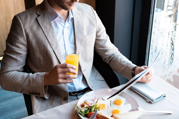 Cropped view of businessman holding glass of orange juice and newspaper in cafe — Stock Photo