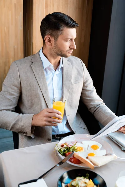 Pensive businessman holding glass of orange juice and newspaper in cafe — Stock Photo