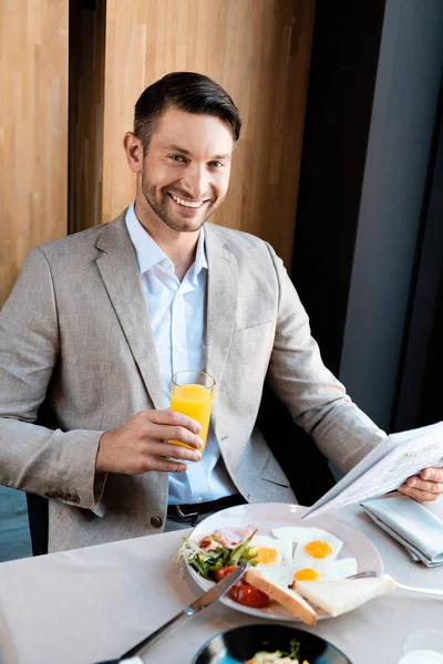 Homme d'affaires souriant tenant un verre de jus d'orange et un journal dans un café — Photo de stock