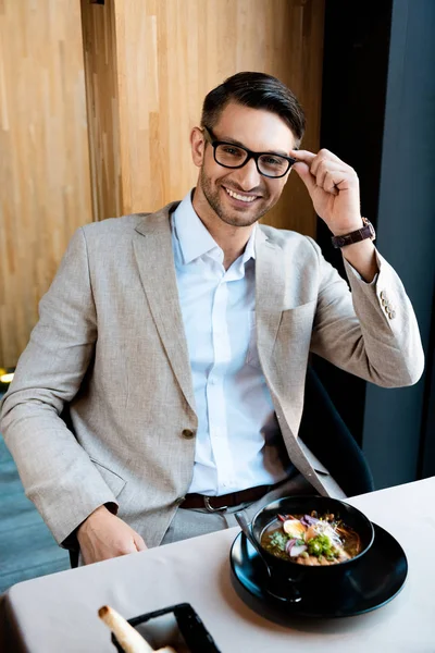 Smiling businessman in glasses looking at camera while sitting at table in cafe — Stock Photo