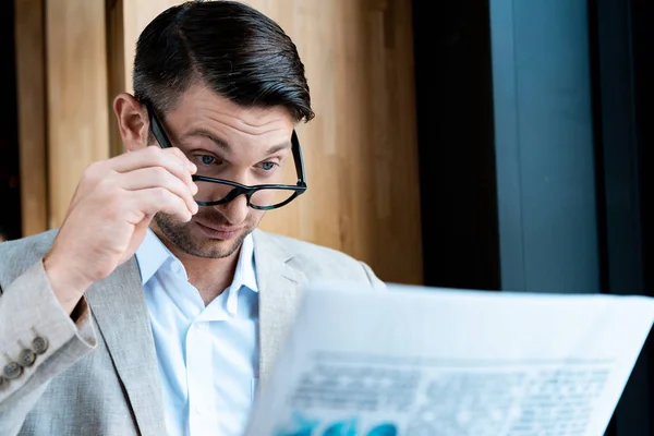 Здивований бізнесмен в окулярах читає газету в кафе — стокове фото