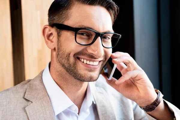 Uomo d'affari sorridente in occhiali che parla su smartphone in caffè — Foto stock