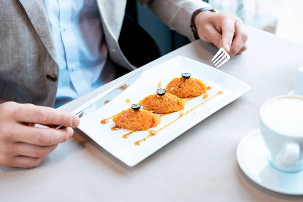 Vista recortada del hombre de negocios sosteniendo tenedor y cuchillo mientras está sentado en la mesa con delicioso plato - foto de stock