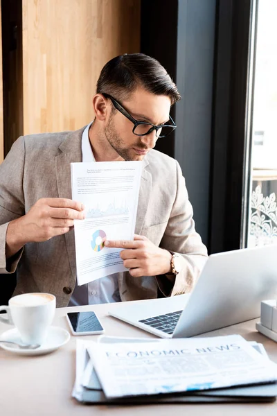 Hombre de negocios en gafas que muestran documento a la pantalla del ordenador portátil en la cafetería - foto de stock