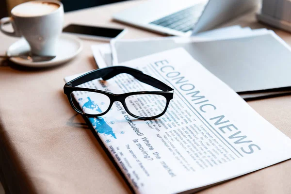 Laptop und Smartphone, Tasse Kaffee, Dokumente, Zeitung und Gläser auf dem Tisch im Café — Stockfoto