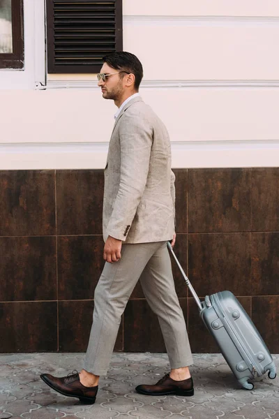 Vue pleine longueur de l'homme d'affaires en lunettes de soleil tenant valise sur la rue — Photo de stock