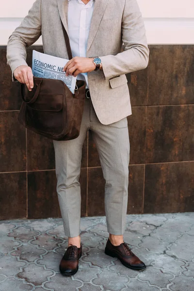Vista ritagliata di uomo d'affari in orologio da polso con giornale in borsa in piedi sulla strada — Foto stock