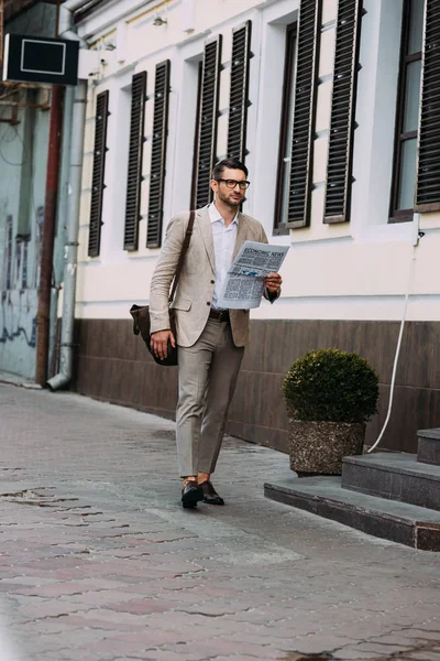 Vista a tutta lunghezza di uomo d'affari concentrato in occhiali leggendo giornale sulla strada — Foto stock