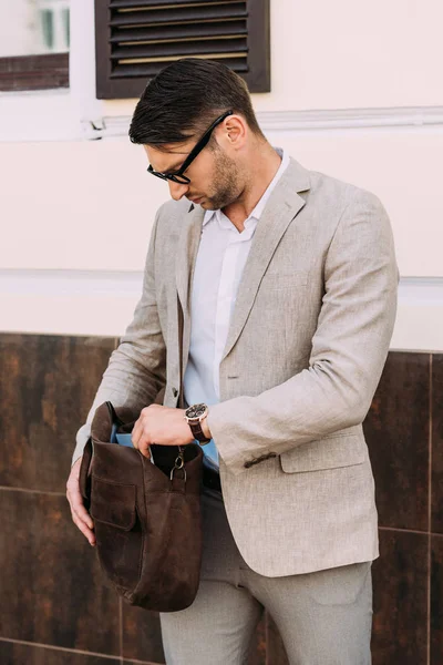 Serious businessman in wristwatch holding leather bag on street — Stock Photo